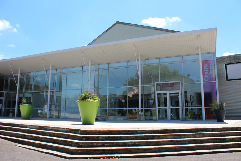 Façade entièrement vitrée du Centre Culturel Jean-Pierre Fabrègue. On y rentre par une esplanade accessible par quelques marches. La façade est protégée du soleil par un débord de toiture supporté par de fins poteaux métalliques peints en blanc.